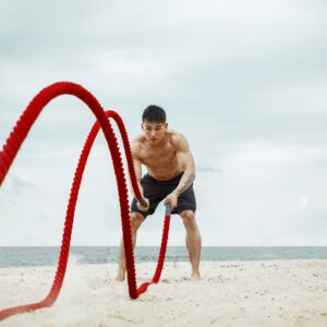 Young healthy man athlete doing exercise with the rope at the beach. Signle male model shirtless training air at the river side in sunny day. Concept of healthy lifestyle, sport, fitness, bodybuilding.
